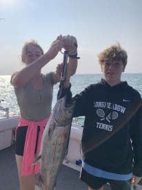 Two young anglers proudly displaying a large fish aboard a fishing charter, showcasing their catch during a day on the water.