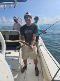 A young adult proudly displaying a caught fish while on a fishing charter, with two others in the background enjoying the day on the water.