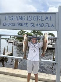 A young angler proudly displaying two Redfish at Chokoloskee Island, showcasing a successful fishing trip.