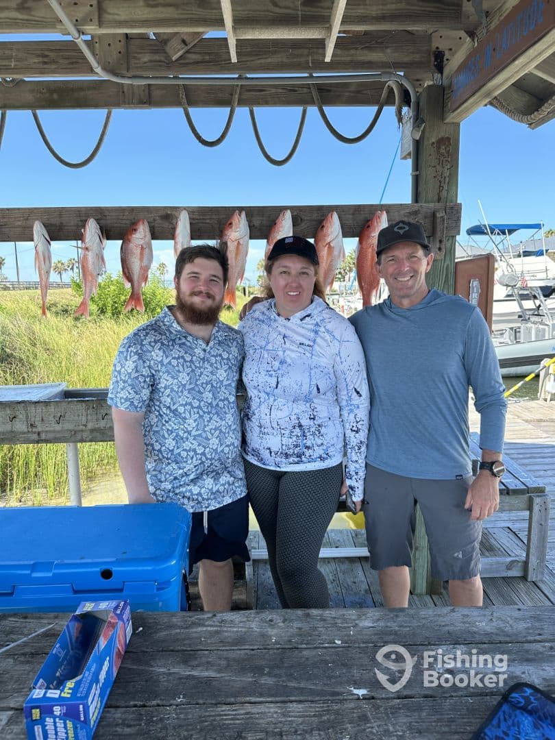A group of three anglers proudly posing in front of a catch board displaying several Red Snapper after a successful fishing trip.