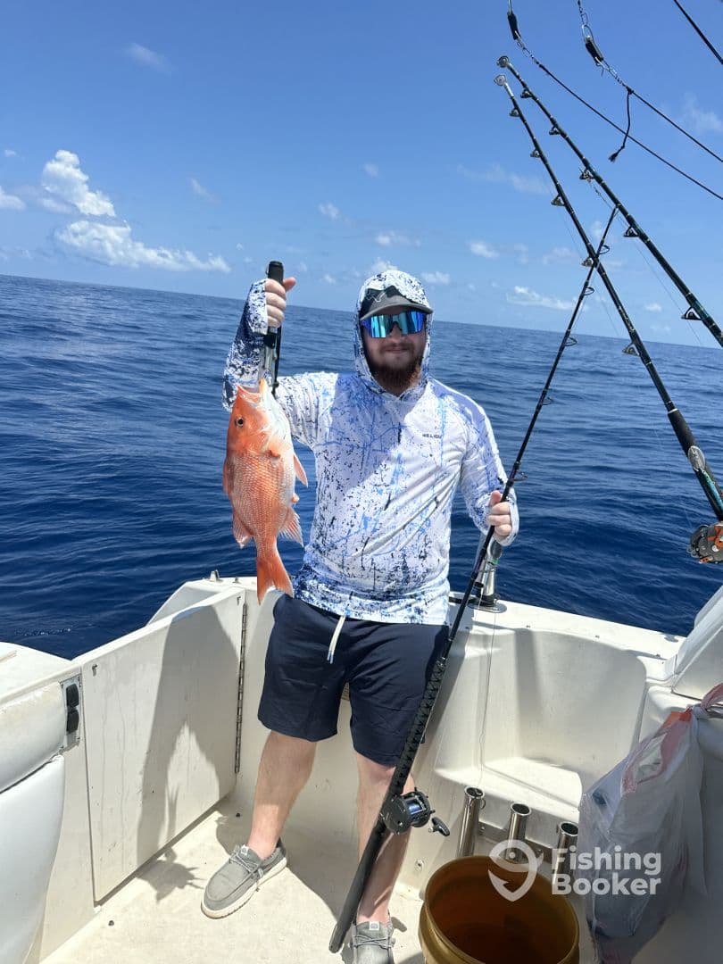Angler holding a vibrant Red Snapper while fishing offshore, showcasing a successful catch on a sunny day.