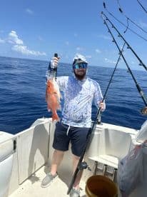 Angler holding a vibrant Red Snapper while fishing offshore, showcasing a successful catch on a sunny day.