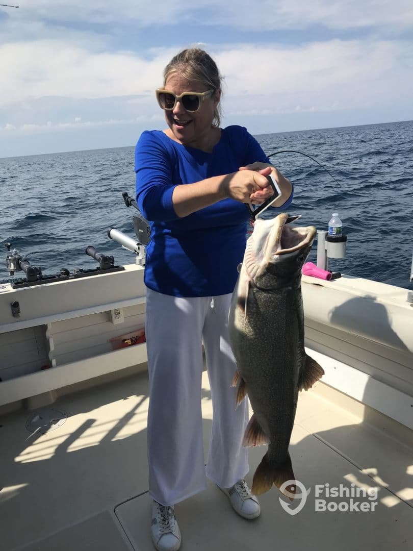 An excited angler holding a large Lake Trout aboard a fishing boat, showcasing a successful day on the water.