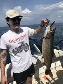 An angler proudly displaying a large Lake Trout while fishing offshore, showcasing a sunny day on the water.