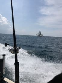 A scenic view of a sailing ship in the distance, captured from a fishing boat while cruising through open waters.