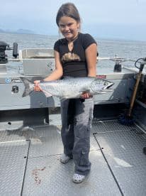A young angler proudly displaying a large Salmon on a fishing boat, showcasing a successful day on the water.