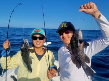 Two anglers proudly displaying their catch of Black Sea Bass while fishing offshore, showcasing a sunny day on the water.