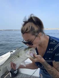 Angler kissing a large striped bass while on a boat, showcasing a personal connection with the catch during a fishing trip.