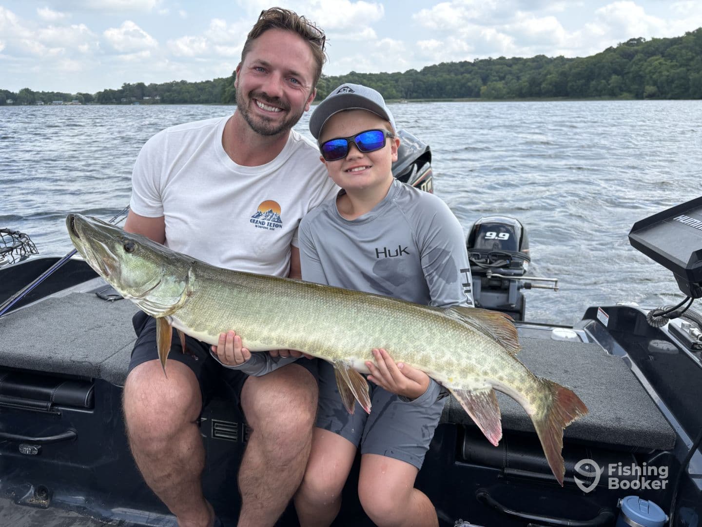 A young angler and an adult proudly displaying a large Muskellunge while fishing on a lake, showcasing a memorable family fishing experience.