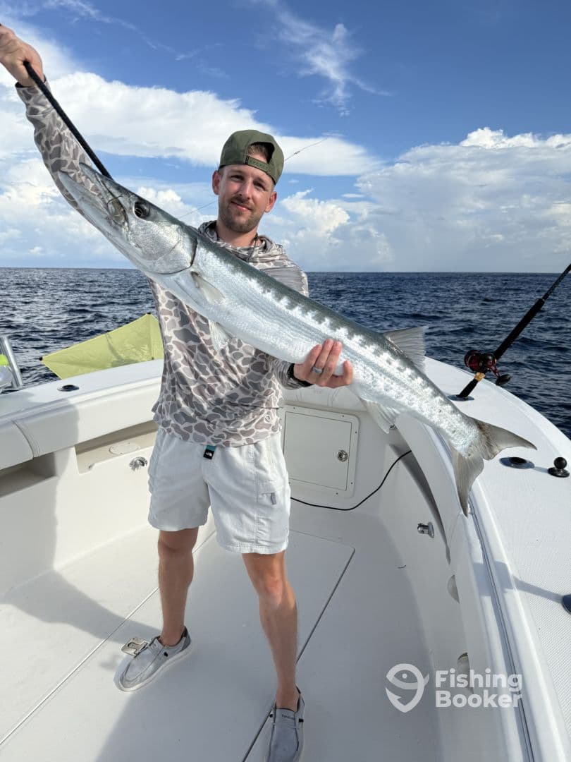 Angler proudly displaying a large Barracuda on a fishing charter in open waters, showcasing a successful day on the boat.