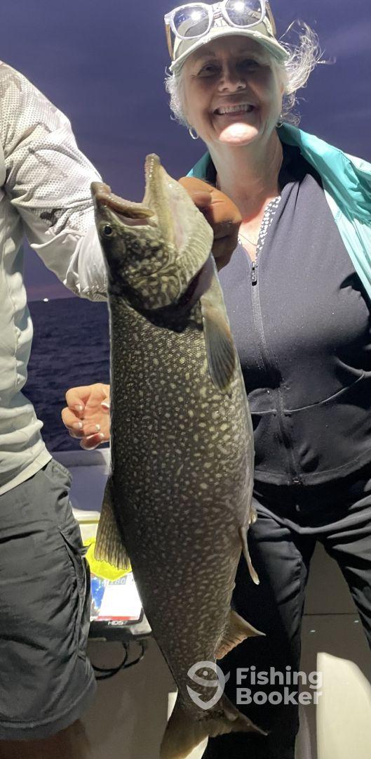 An excited angler proudly displaying a large Lake Trout during a night fishing trip.