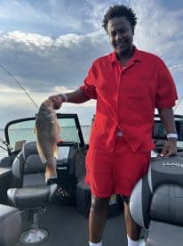 Angler proudly displaying a large Snapper while fishing from a Lund boat, enjoying a sunny day on the water.