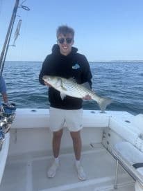 A young angler proudly displaying a striped bass aboard a fishing boat, showcasing a successful day on the water.