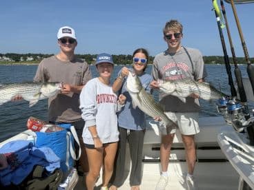 A group of young anglers proudly displaying their catch of striped bass while enjoying a sunny day on the water.