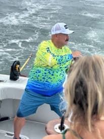 An angler in a vibrant fishing shirt is actively reeling in a catch while on a boat, showcasing the excitement of deep-sea fishing.