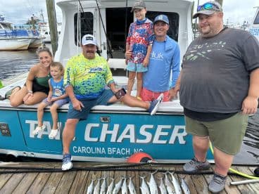 A family poses proudly with their catch of Spanish Mackerel on the dock after a successful fishing trip aboard the 'Tail Chaser' in North Carolina.