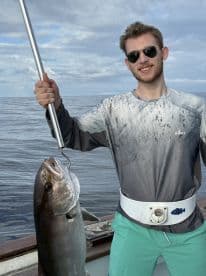 Young angler proudly holding a large fish while fishing offshore, showcasing a successful catch.