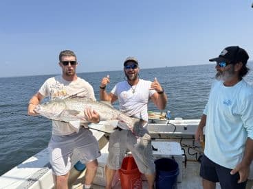 Two anglers proudly displaying a large striped bass on a fishing boat, enjoying a successful day on the water.
