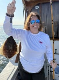 An angler proudly displaying a Flounder while fishing on a boat in calm waters.