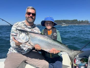 A proud moment for a young angler and his father, showcasing a large Chinook Salmon while fishing off the coast.