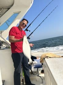 An angler proudly displaying a large Flounder while fishing on a charter boat in open waters.