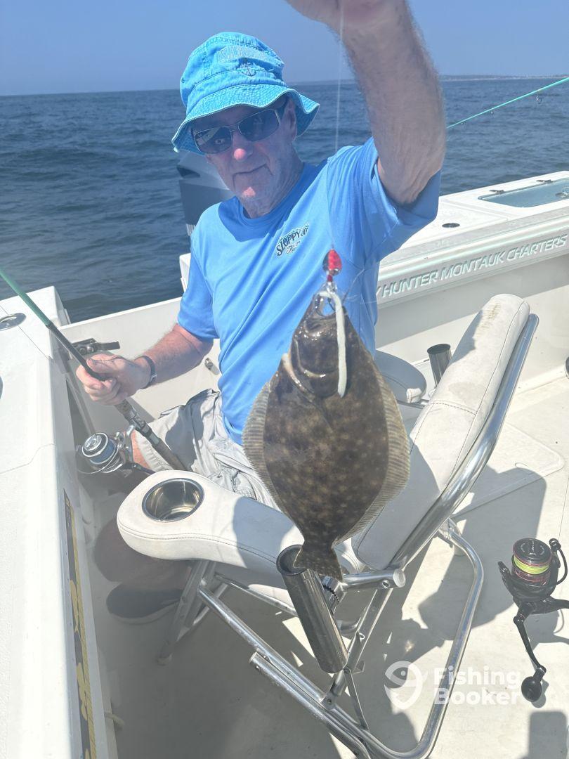 An angler proudly displaying a caught Flounder while seated on a boat, enjoying a day of fishing in open waters.