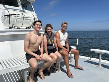 A family enjoying a sunny day on a fishing charter boat, with the ocean in the background.