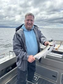 An angler proudly displaying a freshly caught fish while fishing on a boat in open waters, showcasing a cloudy sky.
