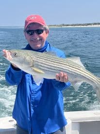 An angler proudly displaying a large Striped Bass while out on the water, showcasing a successful fishing trip.