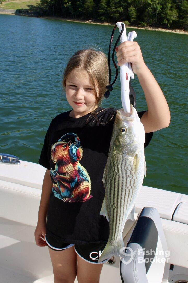 A young angler proudly displaying a striped bass while fishing on a sunny day at the lake.