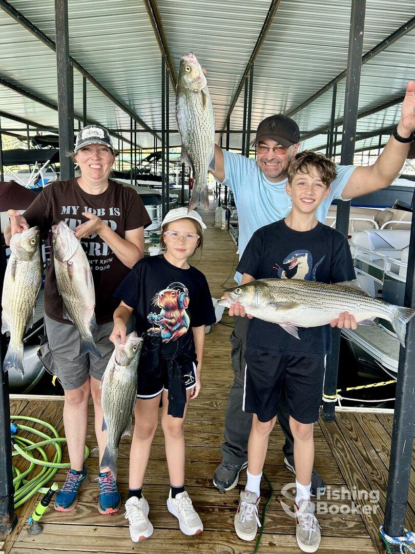 A family proudly displaying their catch of striped bass at a marina, showcasing a successful fishing trip.