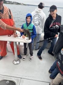 A young boy proudly displays a caught fish while on a fishing charter, surrounded by family members on the boat.