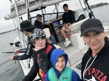 A family enjoying a fishing trip aboard a boat, with a young boy in a life jacket and several anglers preparing to fish.