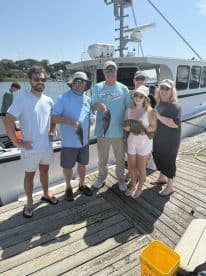 A family group proudly displaying their catch of Flounder on the dock after a successful fishing trip.