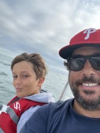 A father and son enjoying a day on the water, captured in a selfie aboard a small fishing boat.