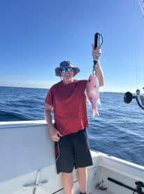 An angler proudly displaying a freshly caught Red Snapper while fishing offshore, showcasing a clear blue sky and calm waters.