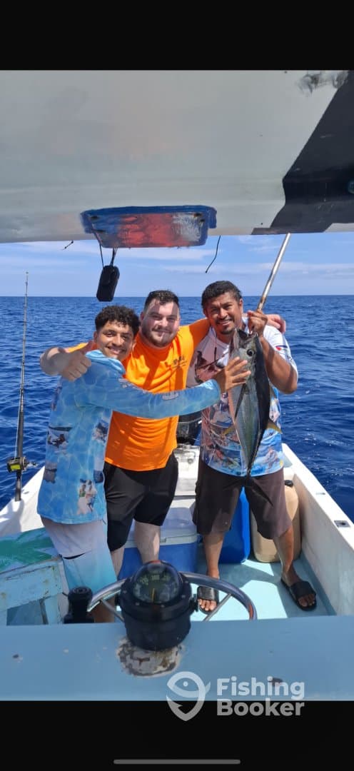 Three anglers celebrating their catch aboard a fishing boat in open water, showcasing a large fish.