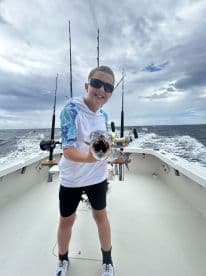 A young angler proudly displaying a large fish on a fishing boat, showcasing the excitement of a deep-sea fishing adventure.