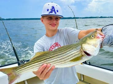 A young angler proudly displaying a striped bass while fishing on a boat, showcasing a successful day on the water.