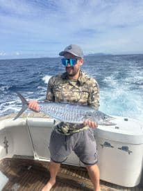 Angler proudly displaying a large Mackerel while aboard a fishing boat in open waters.