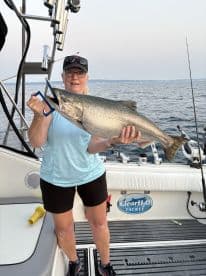 An angler proudly displaying a large Salmon while fishing on a boat, showcasing a successful day on the water.