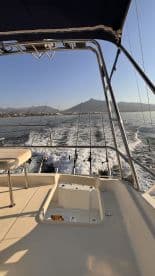 View from the helm of a fishing boat, showcasing multiple fishing rods and a scenic backdrop of mountains and shoreline.