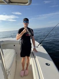 An angler proudly displaying a Black Sea Bass while standing on a boat in calm waters, showcasing a sunny day of fishing.