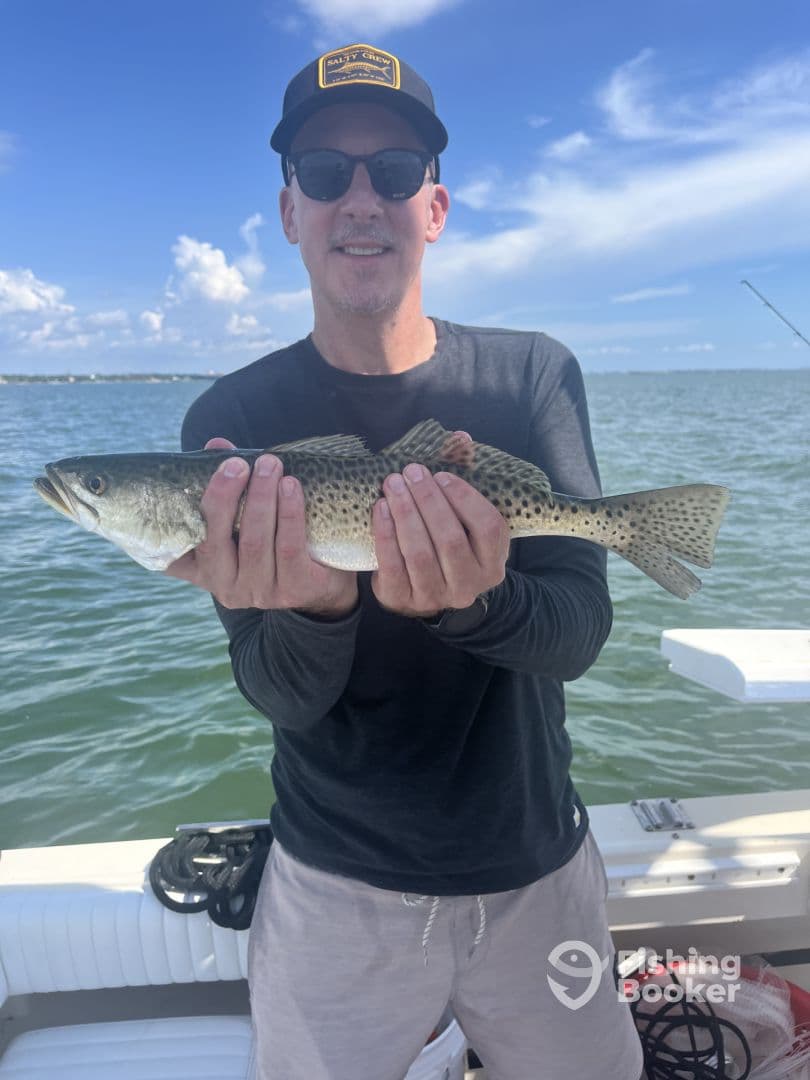 An angler proudly displaying a large Speckled Trout while fishing on a boat in a coastal environment.