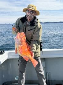 An angler proudly displaying a vibrant Orange Rockfish while fishing in open waters, showcasing a successful day on the boat.