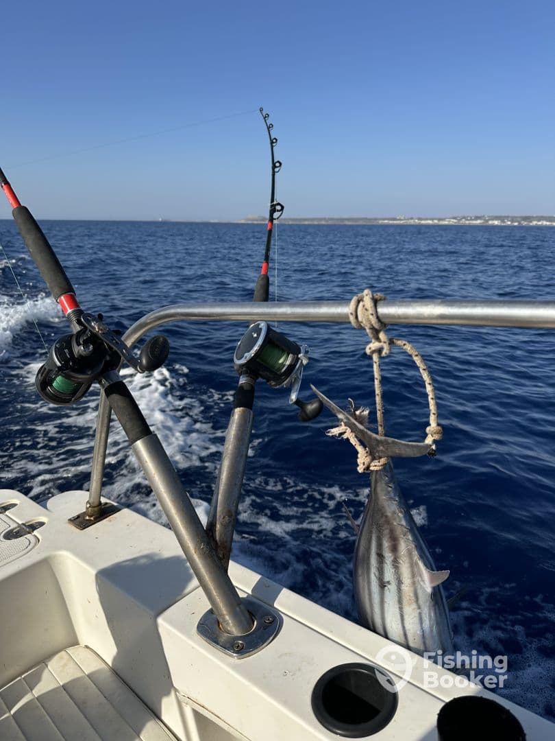 A fishing rod is bent with tension as a fish is being reeled in from the ocean, showcasing an exciting moment on a fishing trip.