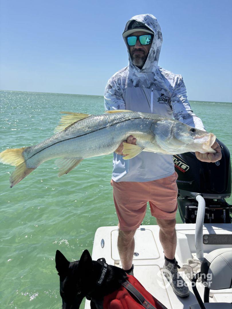 An angler proudly displaying a large Snook while fishing from a boat in clear waters.