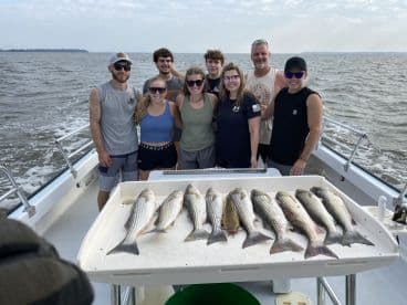 A group of anglers proudly posing on a boat with a display of freshly caught striped bass after a successful fishing trip.