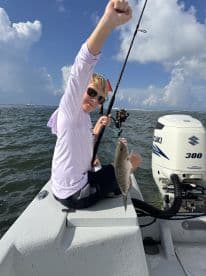 A young angler proudly displaying a caught fish while fishing on a small boat in open waters.