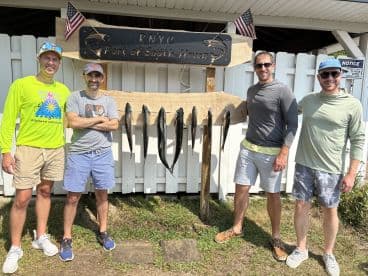 A group of four anglers proudly posing in front of their catch display at a fishing charter in South Haven, showcasing several fish on a board.
